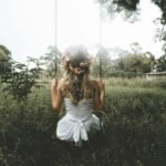 Woman sitting on a swing in a lush garden, wearing a soft flowing dress, capturing a calm and romantic lifestyle moment