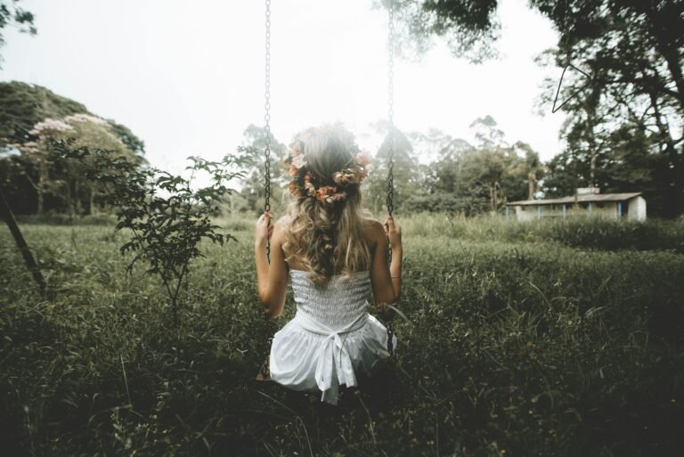 Woman sitting on a swing in a lush garden, wearing a soft flowing dress, capturing a calm and romantic lifestyle moment